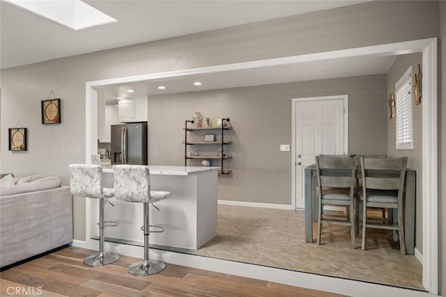 kitchen with a breakfast bar, a skylight, light wood-style floors, stainless steel refrigerator with ice dispenser, and white cabinetry