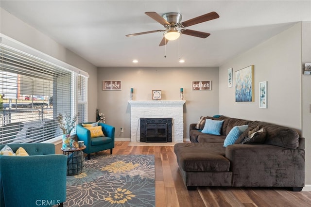 living area featuring a fireplace with flush hearth, a ceiling fan, wood finished floors, recessed lighting, and baseboards