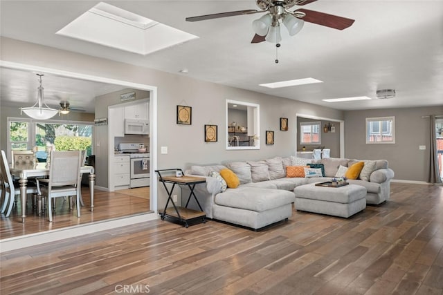 living room featuring a wealth of natural light, baseboards, wood finished floors, and a skylight