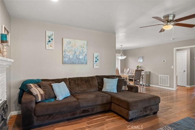 living room with visible vents, a brick fireplace, baseboards, and wood finished floors