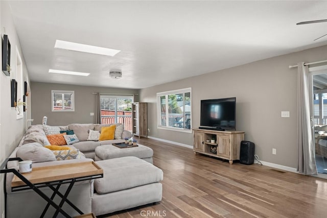 living room with ceiling fan, wood-type flooring, and a skylight