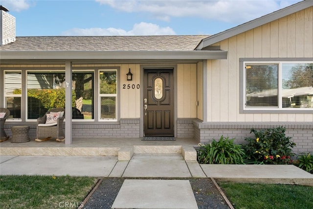 doorway to property with a chimney, roof with shingles, covered porch, and brick siding