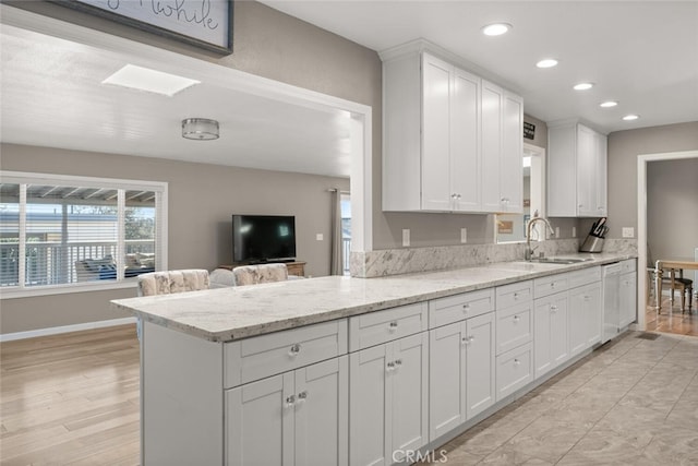 kitchen featuring white cabinetry, kitchen peninsula, white dishwasher, light stone countertops, and sink