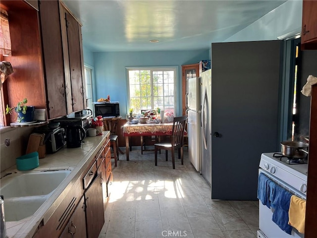 kitchen featuring stainless steel refrigerator, sink, tile countertops, and white gas range oven