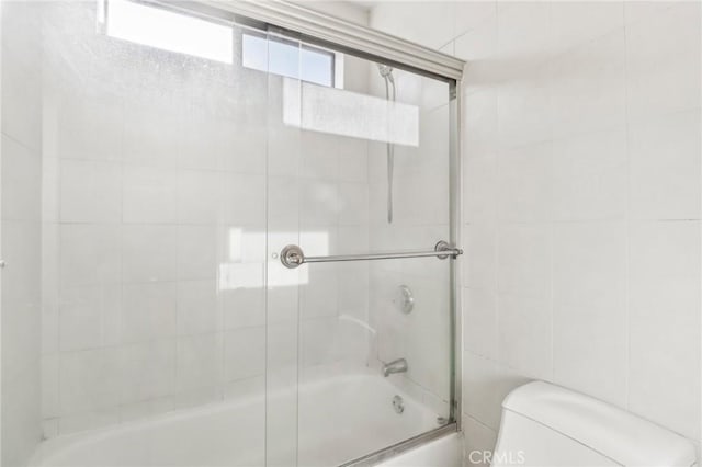 bathroom with toilet, bath / shower combo with glass door, and tile walls