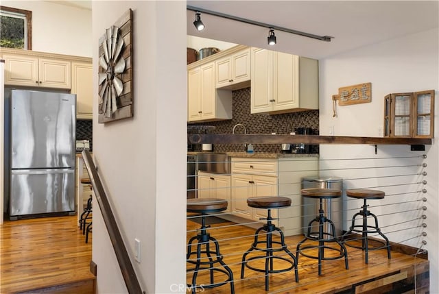 kitchen featuring light hardwood / wood-style floors, tasteful backsplash, cream cabinets, and stainless steel refrigerator