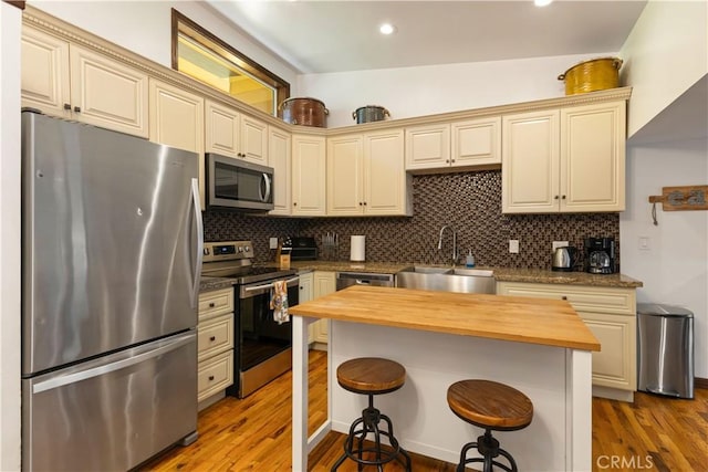 kitchen with cream cabinetry, butcher block countertops, stainless steel appliances, a breakfast bar, and sink