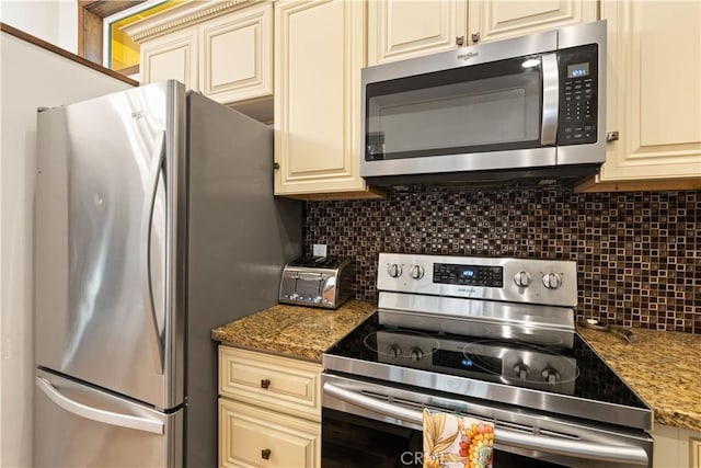 kitchen featuring backsplash, appliances with stainless steel finishes, dark stone counters, and cream cabinets