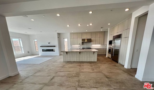 kitchen with a breakfast bar, an island with sink, sink, built in appliances, and light stone countertops