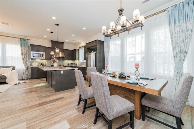 dining room featuring a healthy amount of sunlight, crown molding, light hardwood / wood-style floors, and a notable chandelier