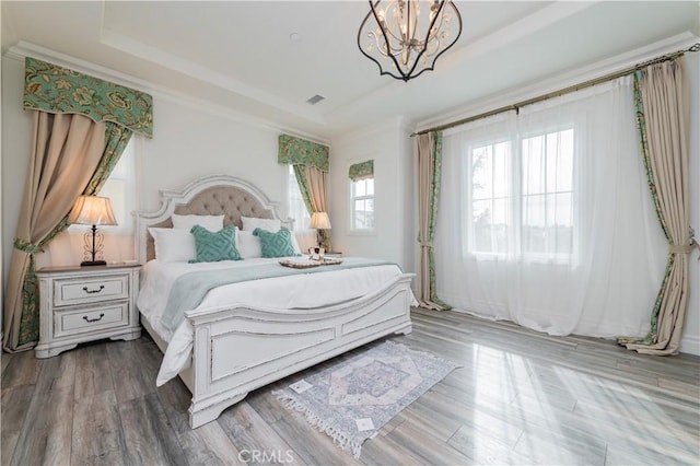 bedroom with wood-type flooring, a tray ceiling, crown molding, and a chandelier