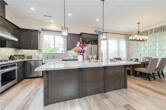 kitchen with decorative light fixtures, a kitchen island, crown molding, appliances with stainless steel finishes, and dark brown cabinets