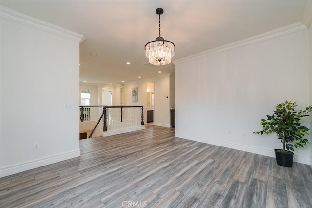 empty room featuring wood-type flooring, ornamental molding, and an inviting chandelier