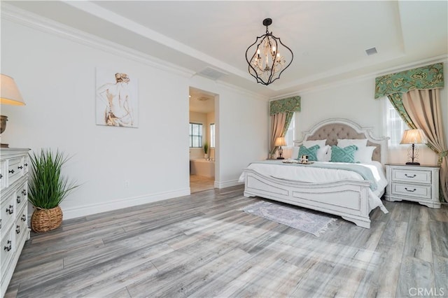 bedroom with an inviting chandelier, light hardwood / wood-style floors, a tray ceiling, ensuite bath, and ornamental molding