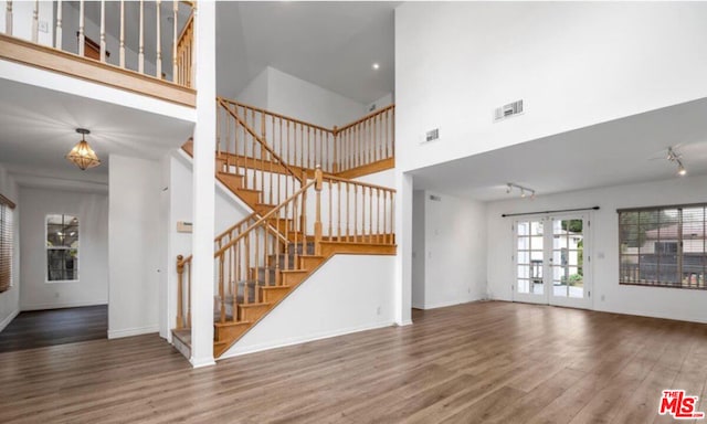 unfurnished living room featuring french doors, a towering ceiling, and hardwood / wood-style floors