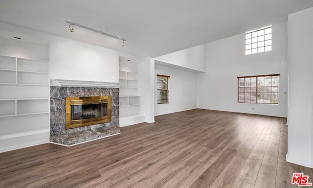 unfurnished living room with built in shelves, a high end fireplace, hardwood / wood-style floors, and rail lighting