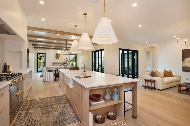 kitchen featuring light hardwood / wood-style floors, light brown cabinets, decorative light fixtures, a kitchen island with sink, and sink