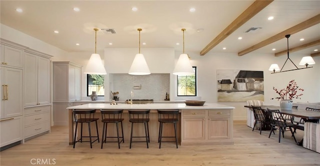 kitchen with pendant lighting, a large island with sink, light wood-type flooring, beam ceiling, and a breakfast bar area