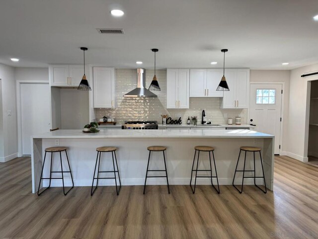 kitchen with white cabinets, a kitchen bar, a spacious island, and wall chimney range hood