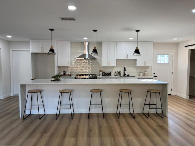 kitchen featuring white cabinetry, a large island, a breakfast bar area, and wall chimney range hood