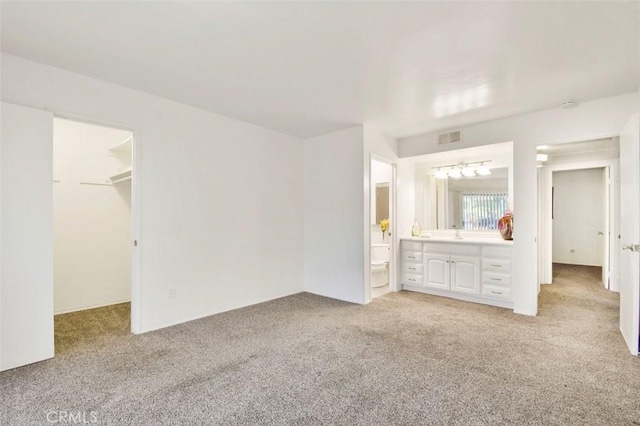 unfurnished bedroom with a walk in closet, a closet, ensuite bath, and light colored carpet