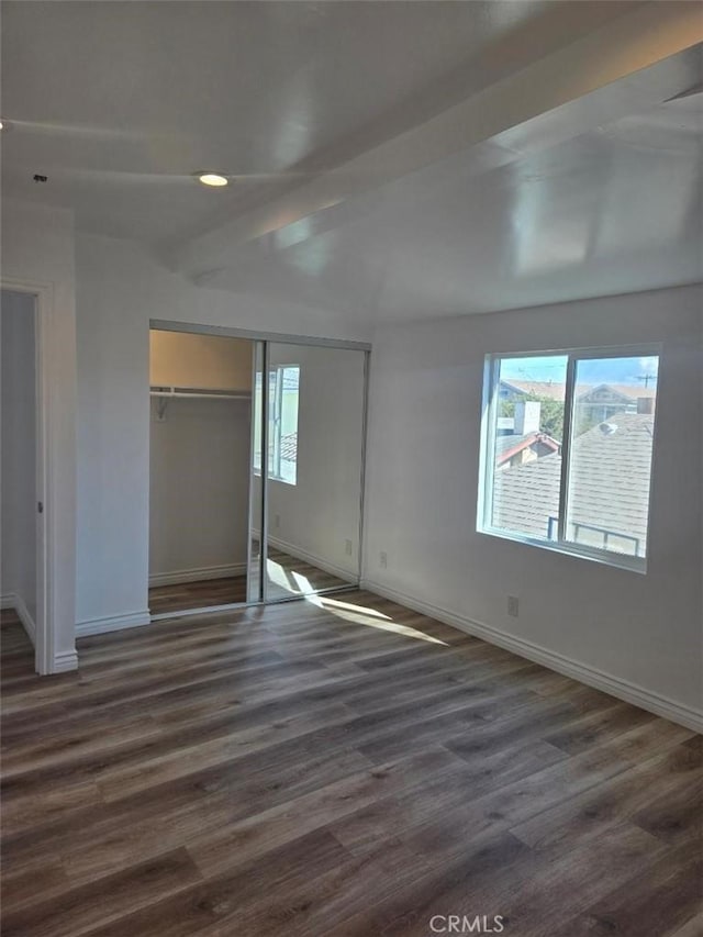 unfurnished bedroom with a closet, dark hardwood / wood-style flooring, and beam ceiling