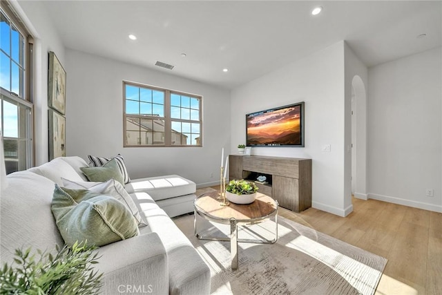 living room with arched walkways, recessed lighting, visible vents, a high end fireplace, and light wood-type flooring