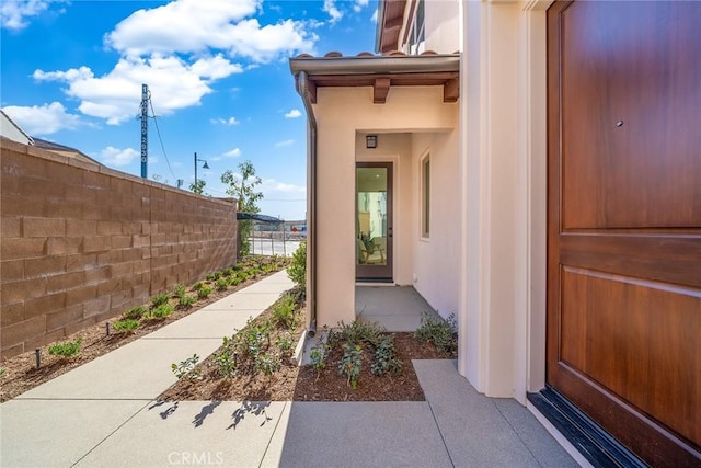 view of exterior entry with fence and stucco siding