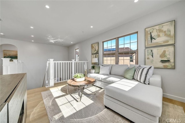 living area with arched walkways, light wood finished floors, baseboards, and recessed lighting