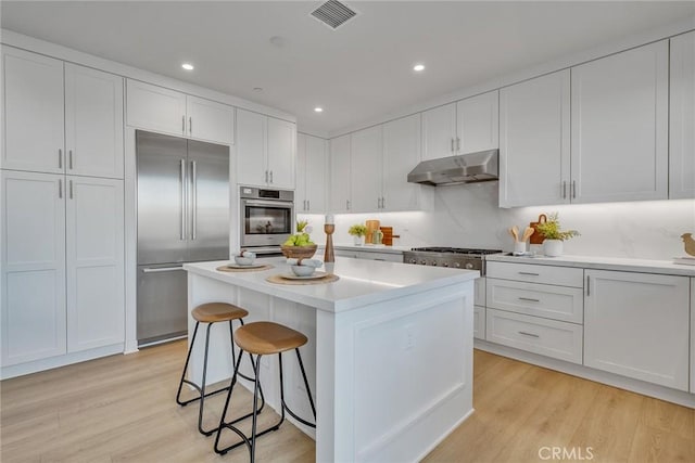 kitchen with a breakfast bar area, visible vents, appliances with stainless steel finishes, white cabinetry, and under cabinet range hood