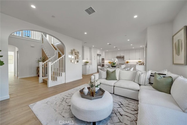 living area with visible vents, arched walkways, stairs, light wood-style floors, and recessed lighting