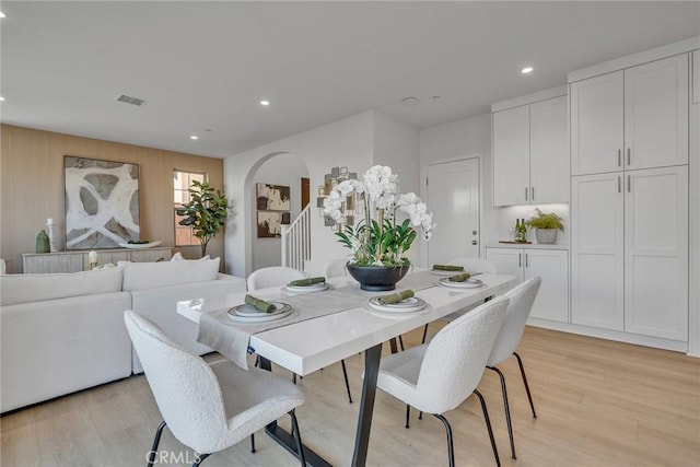 dining room featuring light wood finished floors, visible vents, arched walkways, stairs, and recessed lighting