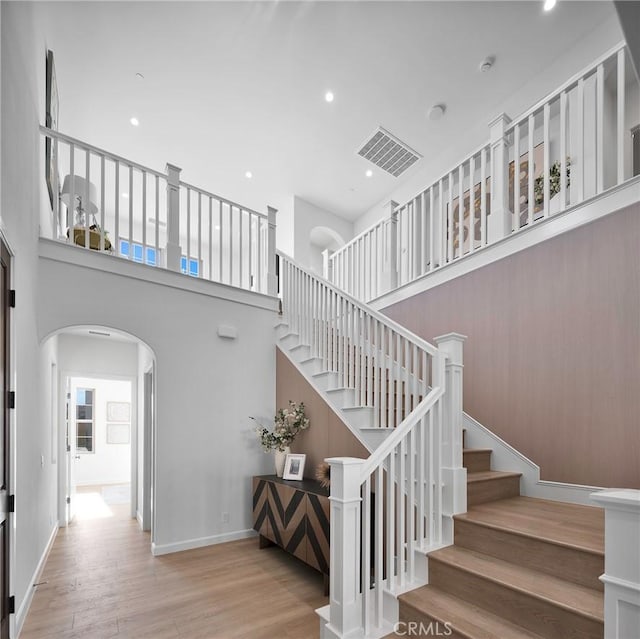 staircase with a towering ceiling, baseboards, arched walkways, and wood finished floors