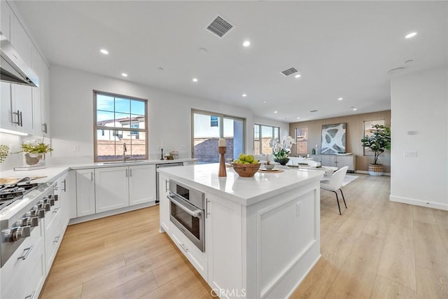 kitchen with extractor fan, a sink, visible vents, stainless steel oven, and light wood-style floors