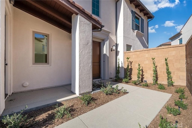 entrance to property featuring a patio area, fence, and stucco siding