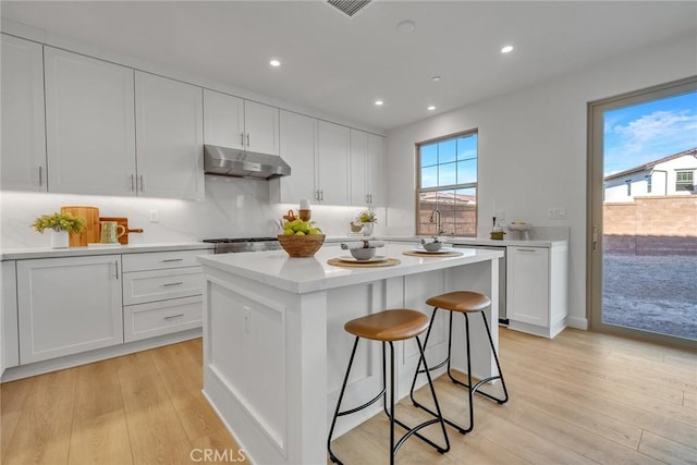 kitchen with a breakfast bar area, under cabinet range hood, a kitchen island, light countertops, and light wood-type flooring