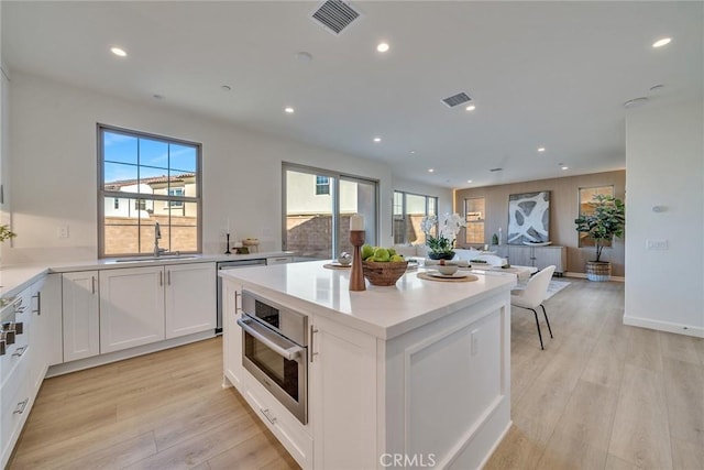 kitchen featuring oven, a sink, visible vents, white cabinets, and light wood-type flooring