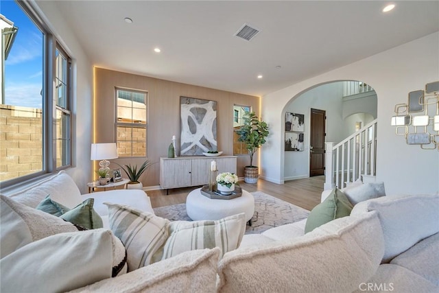 living area featuring light wood-style flooring, visible vents, arched walkways, and recessed lighting