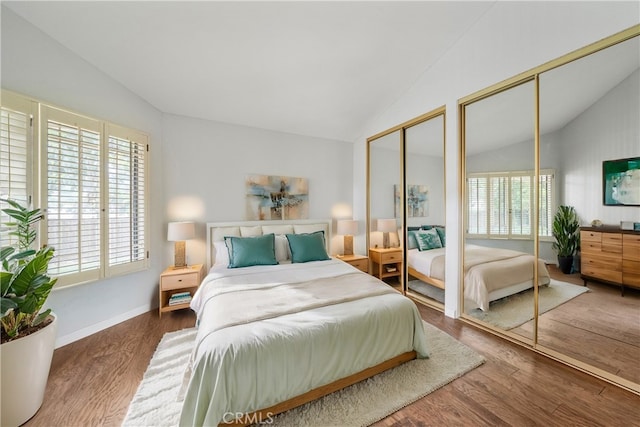 bedroom featuring hardwood / wood-style floors, lofted ceiling, and multiple closets