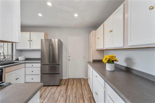 kitchen featuring sink, white cabinetry, light wood-type flooring, and stainless steel refrigerator