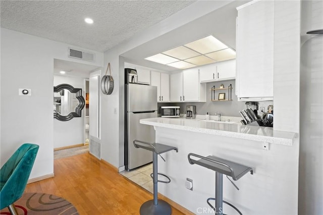 kitchen featuring a kitchen breakfast bar, a textured ceiling, white cabinetry, kitchen peninsula, and stainless steel appliances