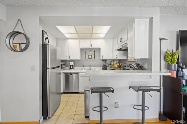 kitchen with a breakfast bar, white cabinets, light tile patterned floors, kitchen peninsula, and stainless steel appliances