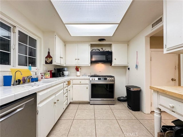 kitchen featuring sink, white cabinetry, tile countertops, light tile patterned floors, and stainless steel appliances