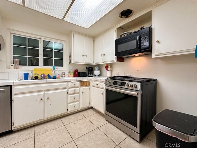 kitchen with light tile patterned flooring, tile counters, white cabinets, and stainless steel gas stove