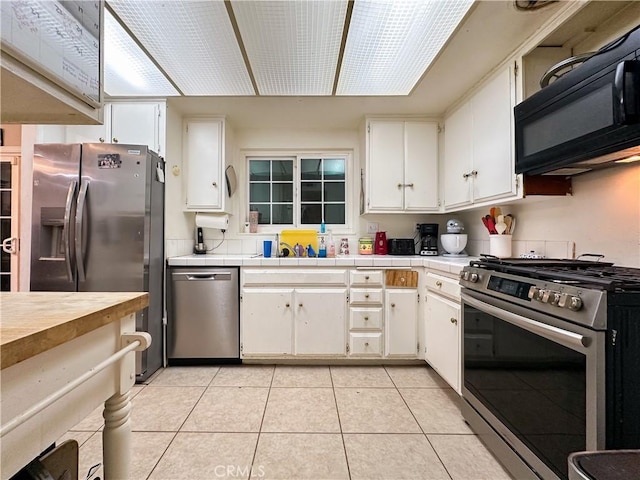 kitchen featuring light tile patterned floors, sink, stainless steel appliances, tile counters, and white cabinets