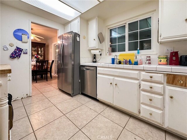 kitchen with white cabinetry, light tile patterned floors, tile counters, and stainless steel appliances