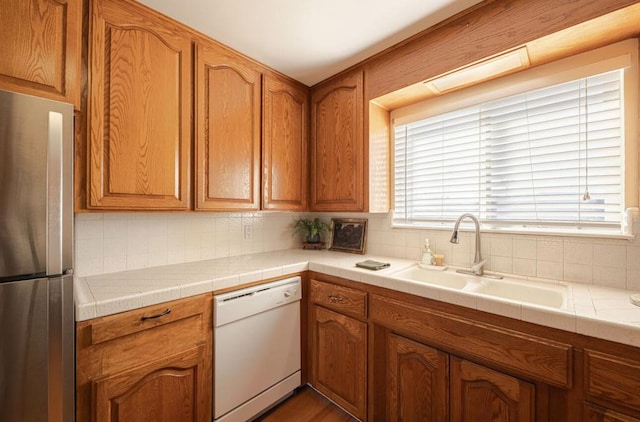 kitchen featuring sink, backsplash, stainless steel fridge, tile countertops, and white dishwasher