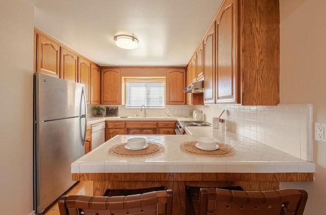 kitchen with a kitchen breakfast bar, kitchen peninsula, dishwasher, and stainless steel refrigerator