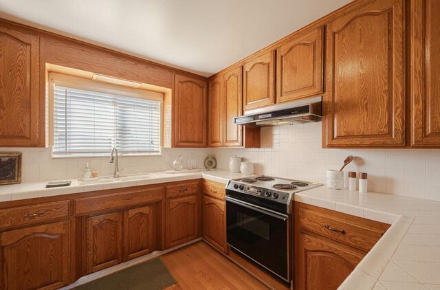 kitchen featuring tile countertops, extractor fan, range with electric cooktop, light hardwood / wood-style flooring, and sink