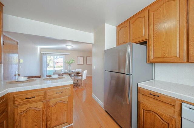 kitchen featuring decorative backsplash, light wood-type flooring, tile countertops, and stainless steel refrigerator